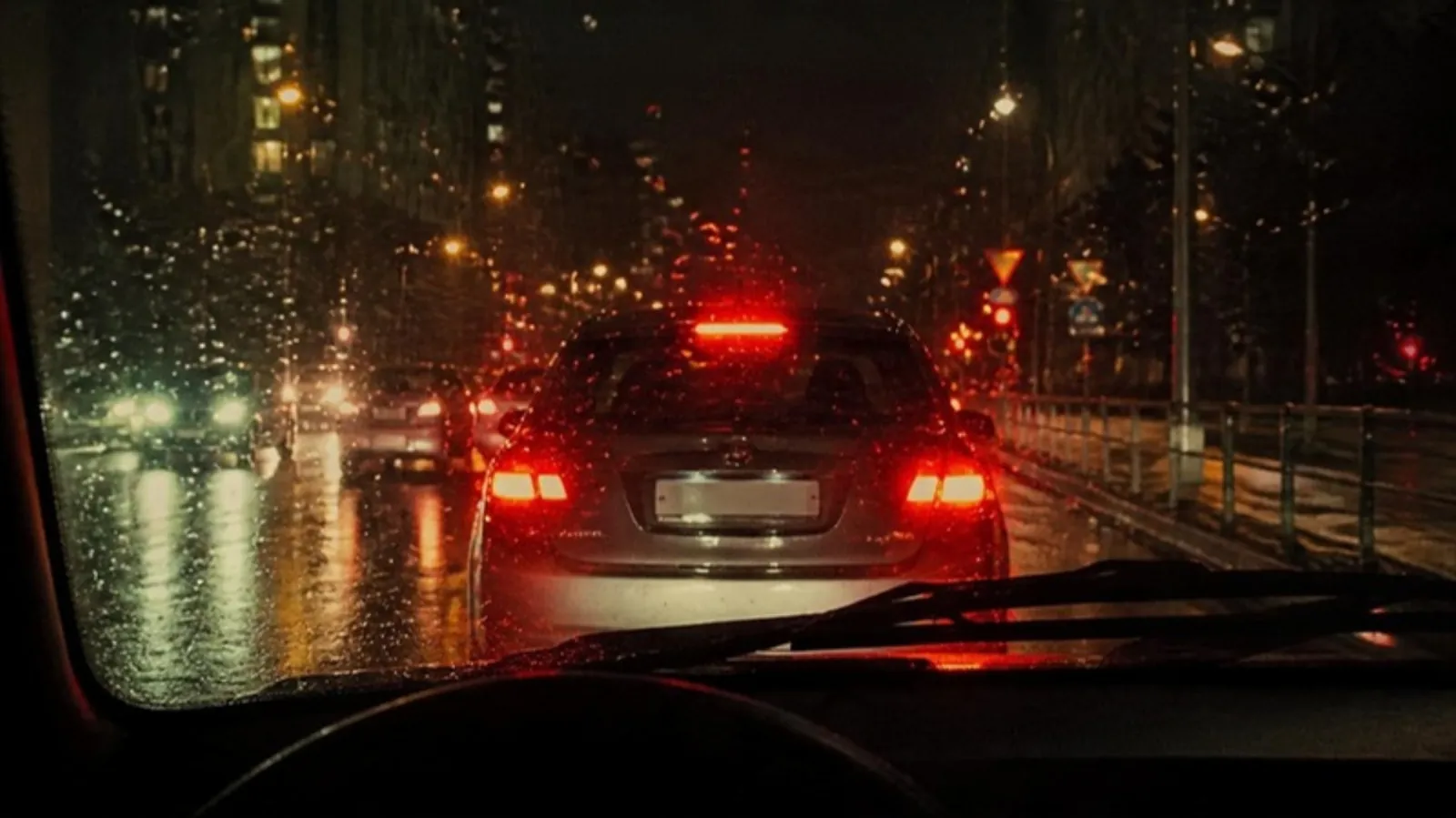 Car tail lights seen through a rainy windshield at night in city traffic