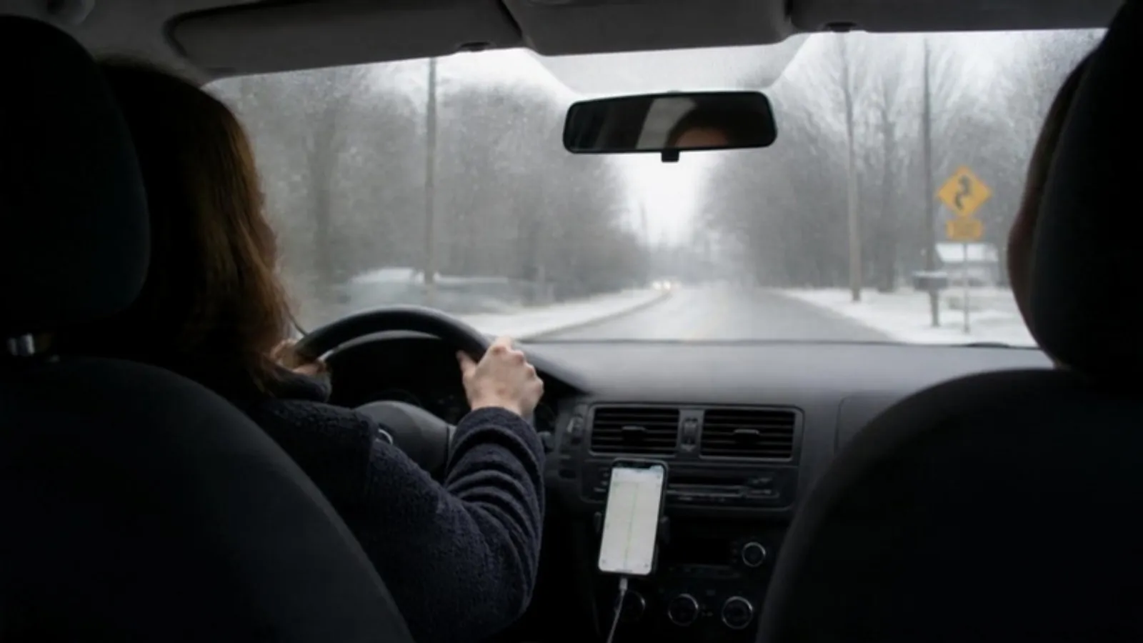 Phone in a dashboard mount showing a map while a driver keeps both hands on the wheel on a snowy road