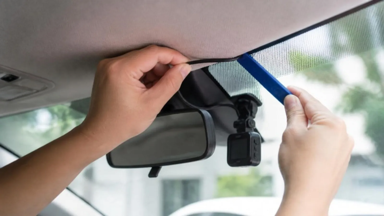Hands tucking a dash cam cable into the headliner with a plastic trim tool